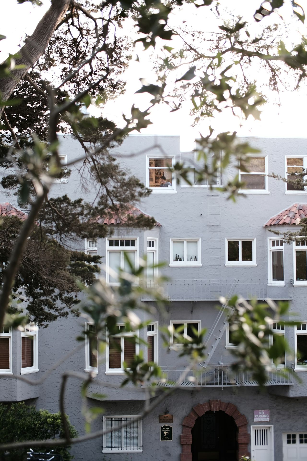 Gray apartment building with trees in the foreground.